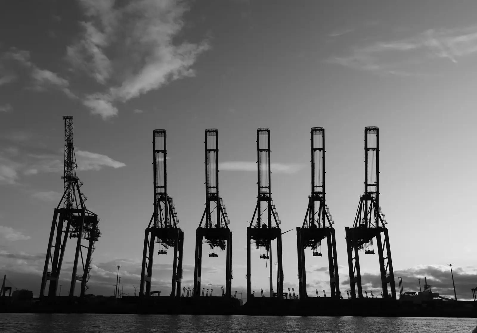 A row of container cranes at a port, against an evening sky